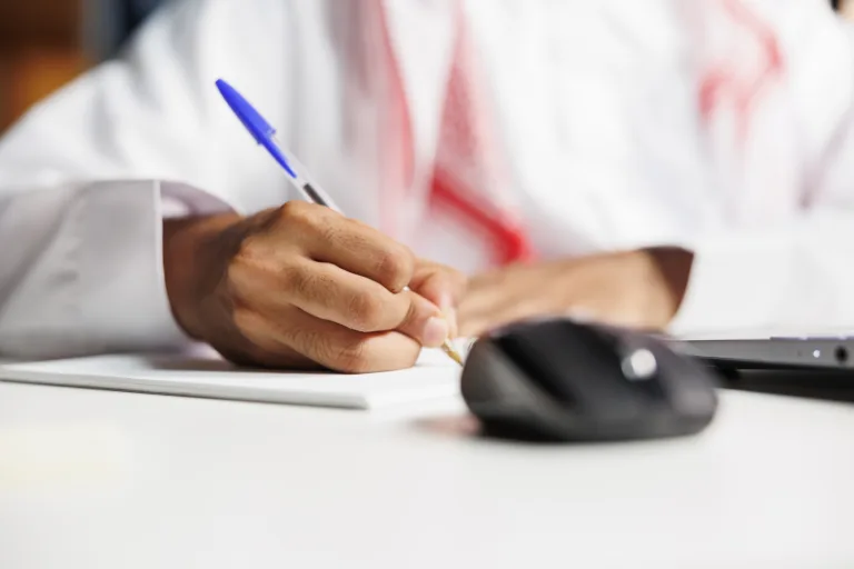 middle eastern freelancer efficiently works his desk scribbling his notebook he conducts online research takes notes stays connected using wireless technology